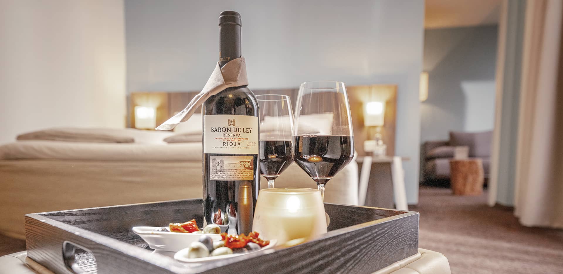 Ein Rotwein mit zwei Gläsern und Snacks auf einem Tablet in einem Sand-Zimmer.